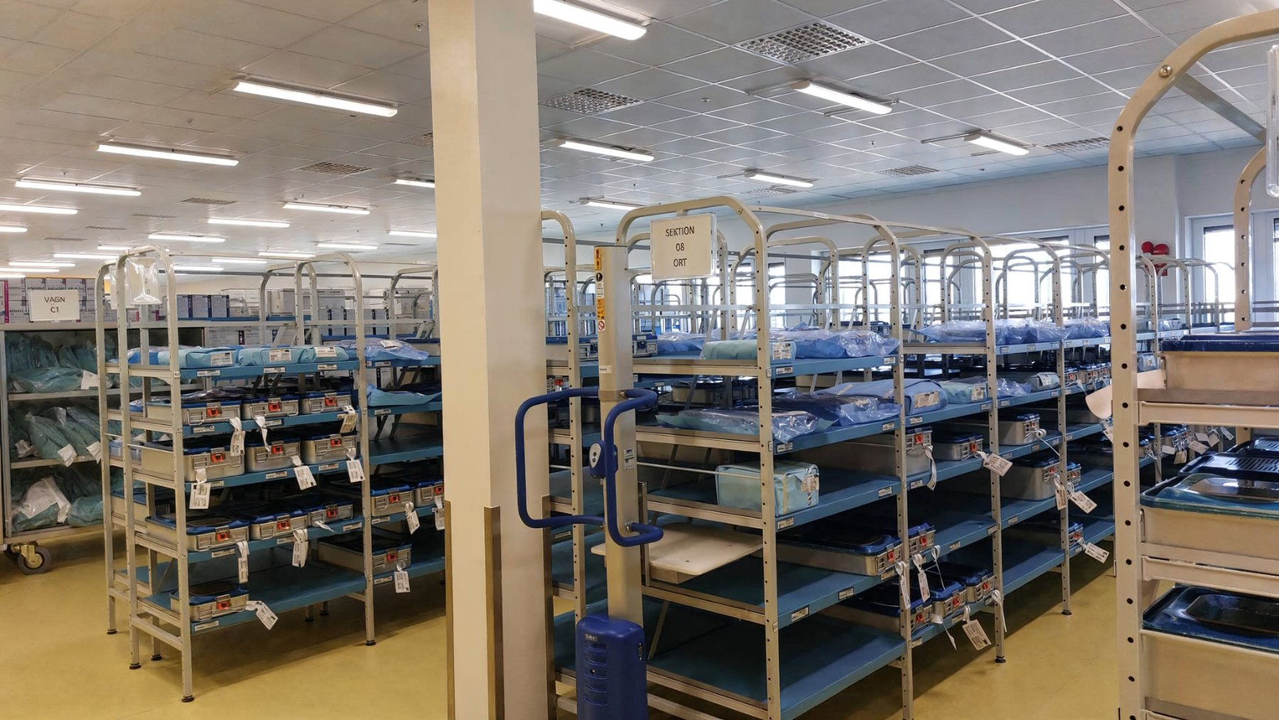 Rows of shelving trolleys holding sterile-wrapped instrument trays in the sterile store.